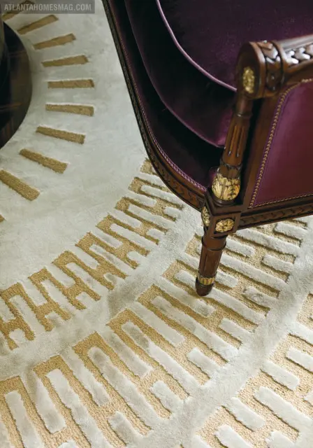 Close-up of a cream rug with a geometric gold pattern and a dark wood chair with purple velvet upholstery and ornate gold accents.