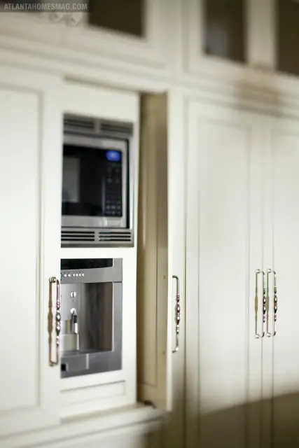 Cream kitchen cabinetry with integrated microwave and coffee maker, featuring ornate silver handles.