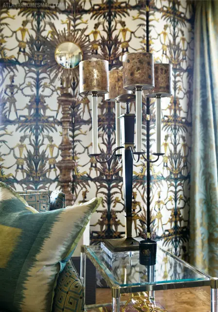 Living room with bold patterned wallpaper, a gold sunburst mirror, a tall candelabra, and a sofa with teal and green ikat pillows.