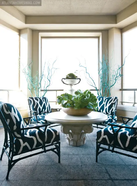 Covered patio with four chairs upholstered in navy and white abstract pattern fabric surrounding a round stone table with a large potted succulent