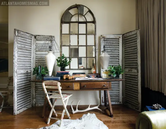 Entryway with antique wooden desk, distressed shutters, arched mirror, and vintage folding chair.