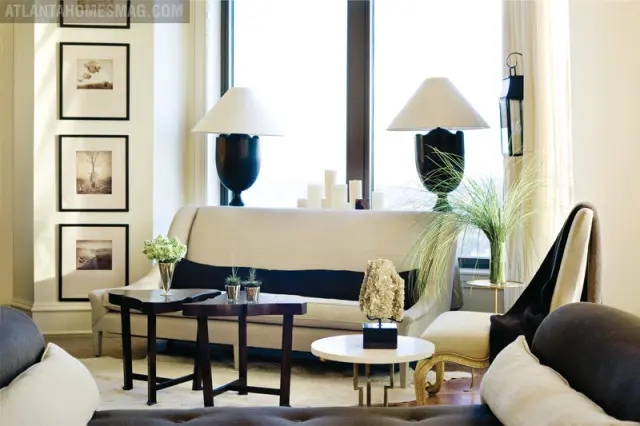 Living room with a neutral-toned sofa, dark wood side tables, and framed art on the wall. Two large lamps flank the sofa, with a vase of tall grass on a side table.