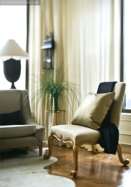 Living room with two upholstered chairs, one with a gold patterned pillow and navy throw, and a floor lamp.