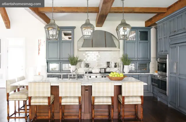 Gray kitchen with marble island, plaid bar stools, white subway tile backsplash, stainless steel appliances, and exposed wooden beams on the ceiling.