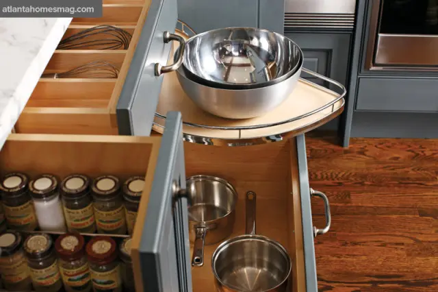 Gray kitchen cabinets with open drawers revealing spice jars, whisks, mixing bowls, and small saucepans.