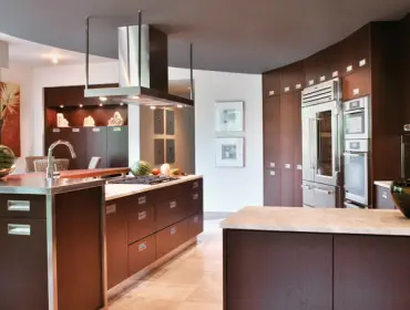 Modern kitchen with dark wood cabinetry, stainless steel appliances, marble countertops, and a large central island with a gas range.