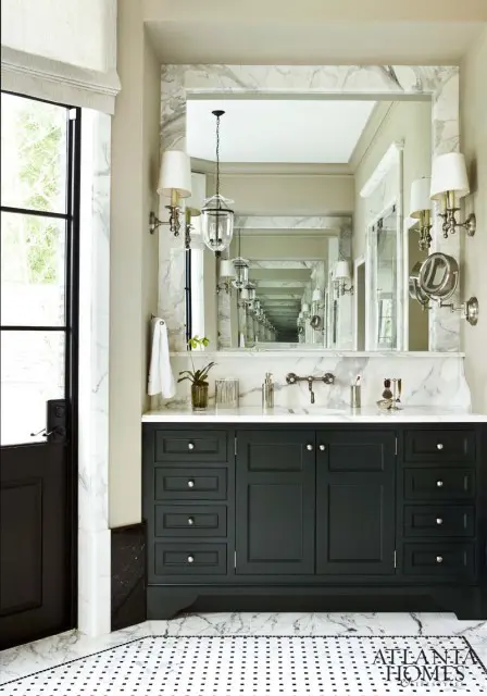 Dark green vanity with marble countertop and backsplash, flanked by sconces and a large mirror reflecting a series of identical vanities.