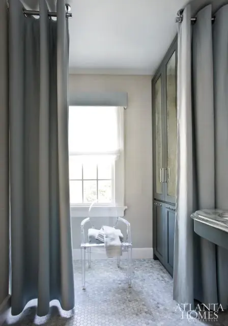 Grey bathroom with hexagonal marble floor, clear acrylic chair with towels, and a tall grey cabinet with mirrored doors.