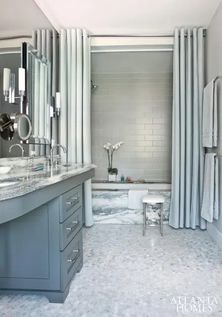Gray bathroom with marble vanity, hexagonal floor tiles, subway tile shower walls, and light blue curtains around the bathtub.