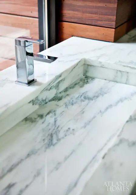 Chrome faucet on a white marble countertop with gray veining. Wooden panels are visible in the background.