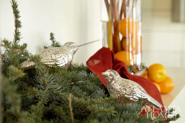 Two silver bird ornaments rest on a Christmas tree branch, with oranges and a red ribbon in the background.