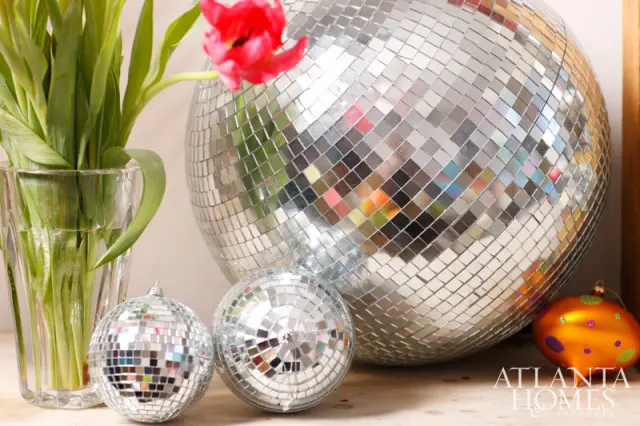 Close-up of a large disco ball and two smaller disco ball ornaments next to a vase of green tulips and a single red tulip.