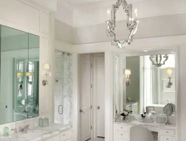 White bathroom with marble hexagonal floor, vanity with marble countertop, mirrored medicine cabinet, glass-enclosed shower, and a vanity table with a tufted stool.