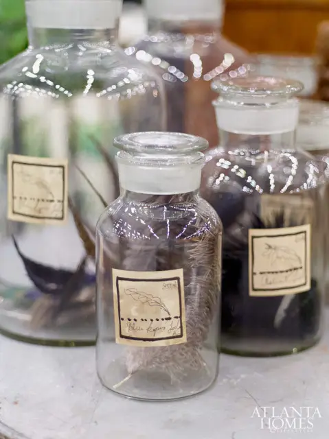 Clear glass apothecary jars filled with various feathers, each with a handwritten label. A watermark for Atlanta Homes & Lifestyles is visible.