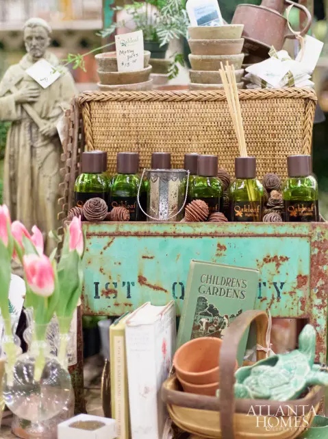 Display of garden items including pink tulips, green bottles, pinecones, terracotta pots, and books, with a statue in the background. A logo for Atlanta Homes & Lifestyles is visible in the lower right corner.
