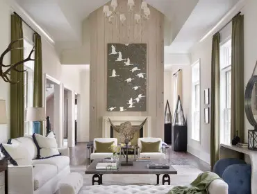 Living room with white sofas, dark wood coffee table, and a large painting of birds above a fireplace. Green curtains frame windows on either side.