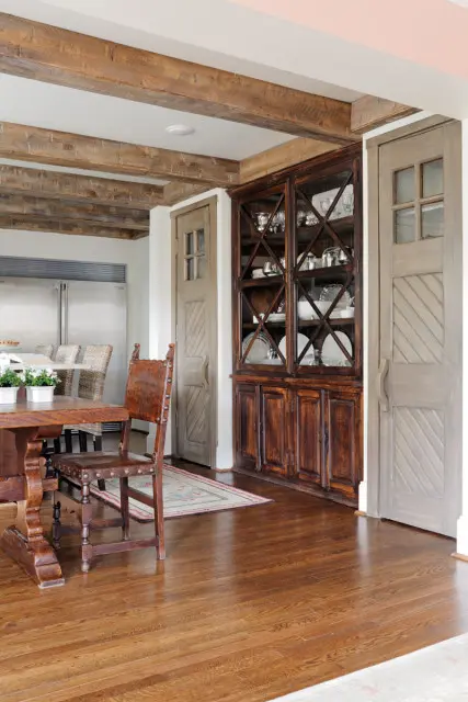 Rustic dining room with dark wood table and chairs, a tall dark wood china cabinet, and distressed gray doors.