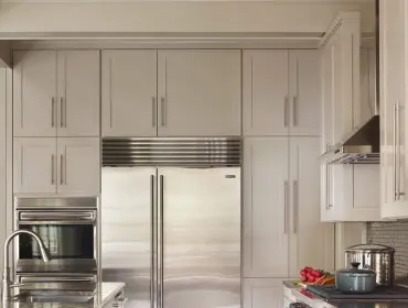 Gray and white kitchen with stainless steel appliances, including a double-door refrigerator, built-in oven, and range. Features include marble countertops, dark wood floors, and shaker-style cabinetry.