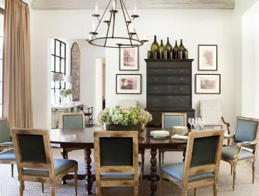Dining room with dark wood oval table, upholstered chairs in blue and cream, dark wood buffet, and a wrought iron chandelier.