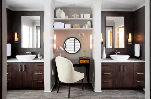 Double vanity bathroom with dark wood cabinets, white vessel sinks, marble countertops, and a central dressing area with a vanity table and chair.