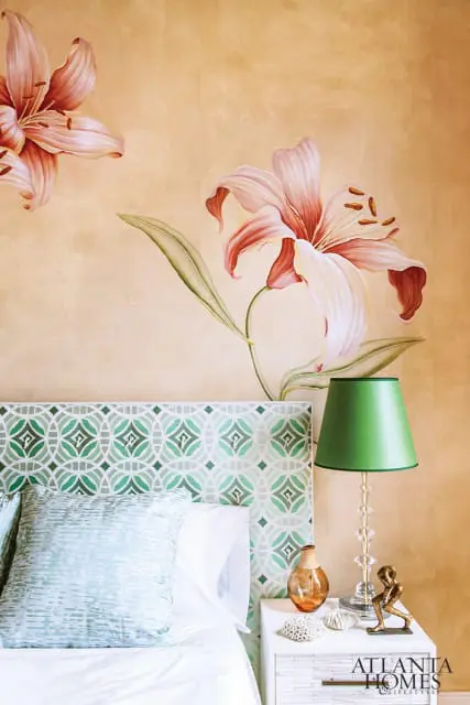 Bedroom with a large floral mural on a textured gold wall, a green patterned headboard, and a green lampshade on a white nightstand.