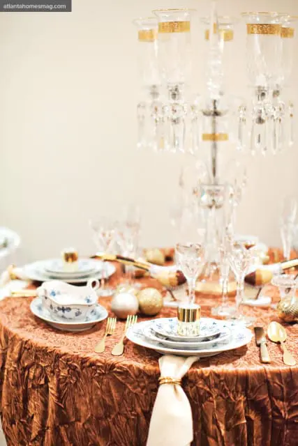 Formal dining table set with a crushed copper tablecloth, blue and white china, gold cutlery, crystal glassware, and gold and silver ornaments.