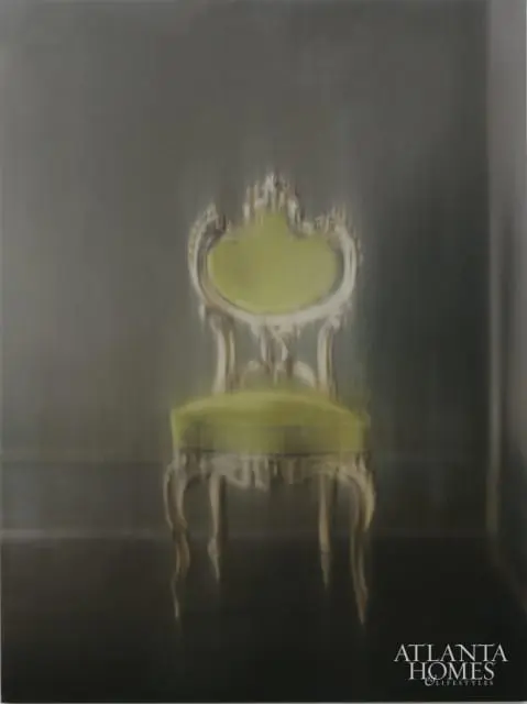 Ornate antique chair with green velvet upholstery and gilded wood frame against a dark gray wall.
