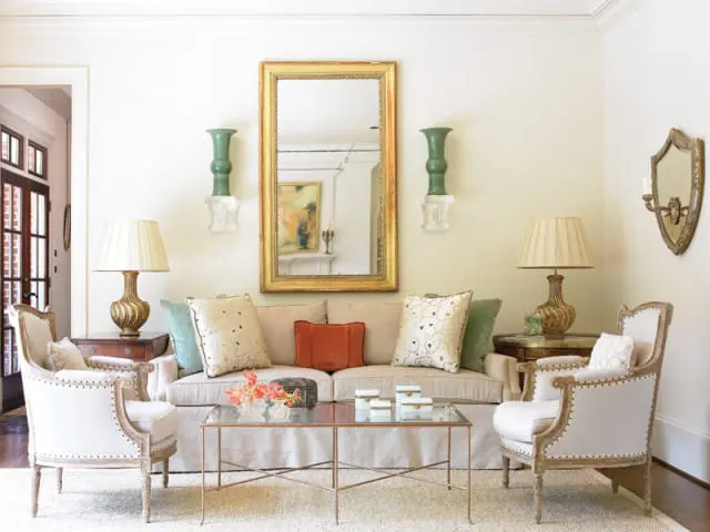 Living room with a neutral-toned sofa and two armchairs, a glass-top coffee table, and decorative wall sconces and mirrors.