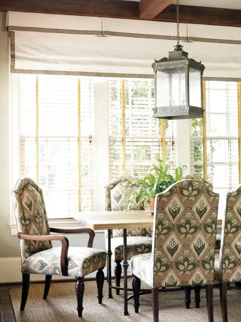 Dining room with upholstered chairs featuring a botanical pattern, wooden table, and a large lantern chandelier hanging from exposed beams.