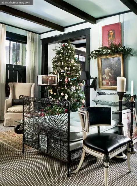 Living room with a decorated Christmas tree, upholstered armchair, black metal daybed with light blue mattress, and ornate black chair with leather seat.