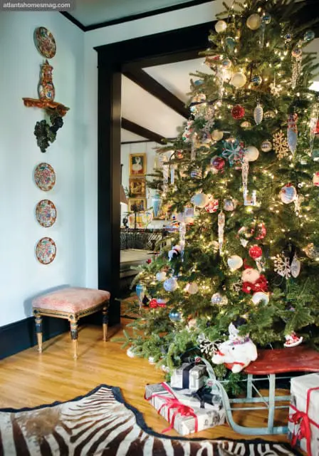 Living room decorated for Christmas with a lit tree, presents, a zebra rug, and decorative plates on the wall.