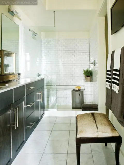 Modern bathroom with dark wood vanity, white subway tile shower, glass enclosure, and a cowhide bench.