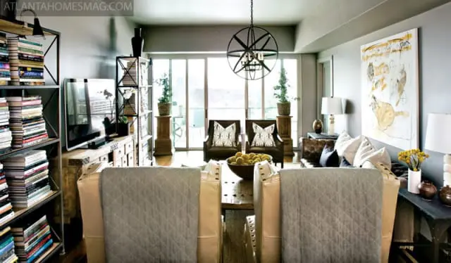 Living room with gray walls, large windows, a metal chandelier, leather armchairs with patterned pillows, and a large abstract painting.