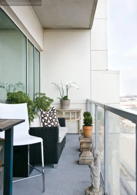 Balcony with gray carpet, black wicker sofa with patterned pillows, white orchids, and a Buddha statue.