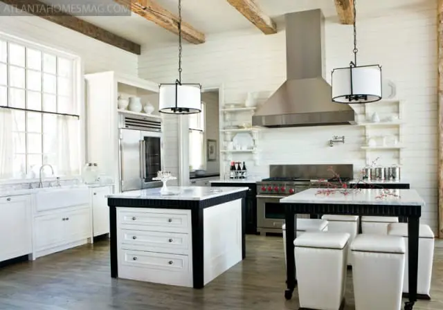 White shiplap kitchen with exposed wooden beams, stainless steel range hood, farmhouse sink, and two marble-topped islands with white seating.