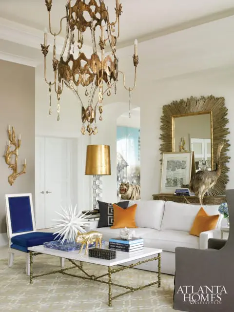 Living room with a white sofa, white marble coffee table with gold legs, blue velvet chair, and a large ornate gold chandelier.