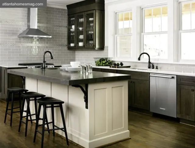 Gray subway tile backsplash in a kitchen with dark wood cabinets, a white island with black stools, and a stainless steel dishwasher.