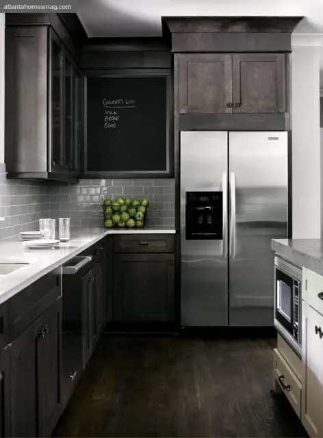 Dark wood kitchen cabinets with a stainless steel refrigerator, subway tile backsplash, and a chalkboard with a grocery list.