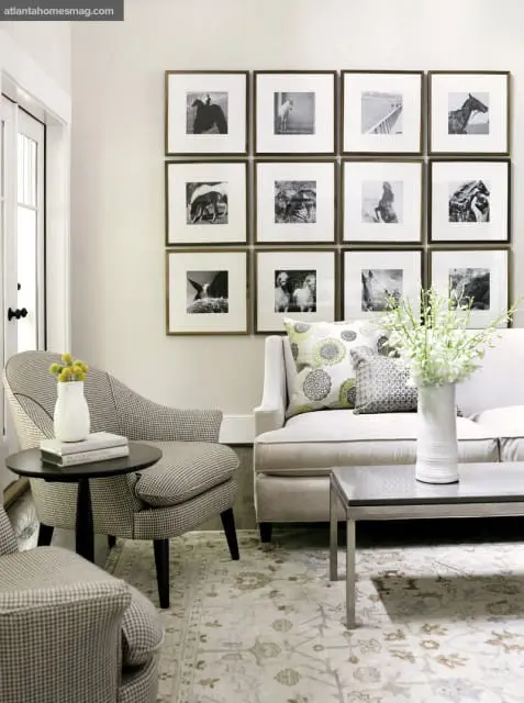 Living room with a gallery wall of twelve framed black and white horse photographs above a neutral sofa and patterned armchairs.