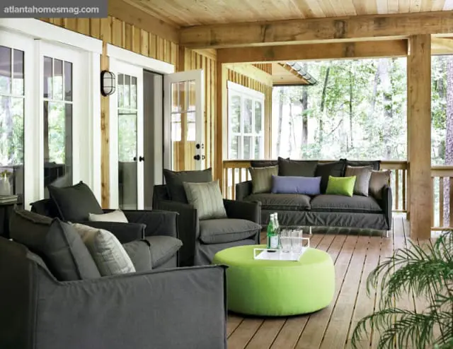 Covered porch with dark gray upholstered seating, a bright green ottoman coffee table, and French doors opening to a wooded area.