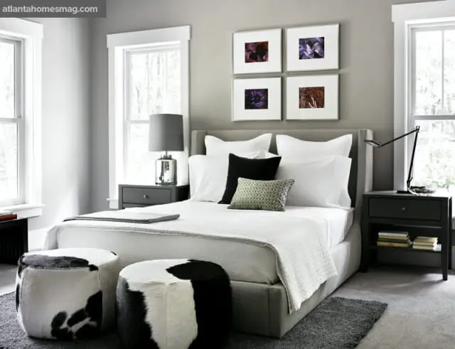 Gray upholstered bed with white linens and black accent pillows, flanked by dark nightstands. Four framed floral prints hang above the bed.