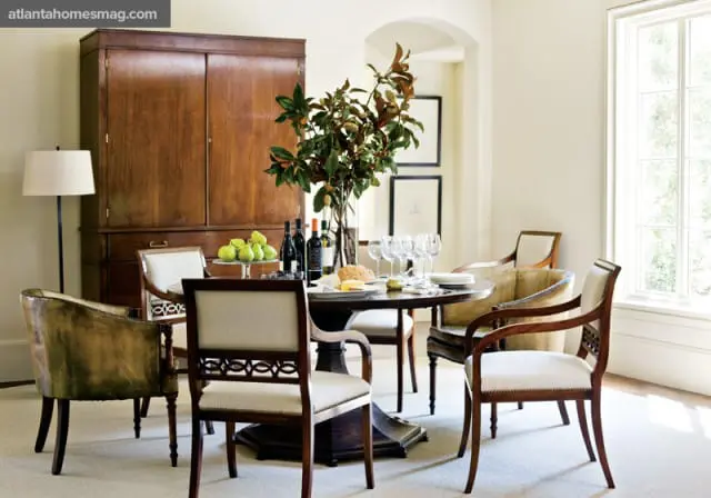 Dining room with a round wooden table set for a meal, surrounded by upholstered chairs and a tall wooden cabinet.