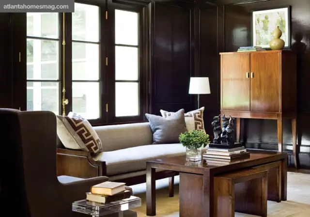 Dark wood paneled living room with a light gray sofa, Greek key patterned pillows, a dark wood coffee table, and a tall wooden cabinet.