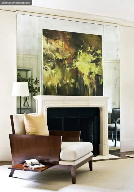 Living room with a cream fireplace, abstract art, and a dark wood armchair with cream upholstery and a yellow accent pillow.