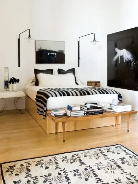 Bedroom with a platform bed, black and white striped blanket, two black wall-mounted sconces, and artwork including a white horse on black background.