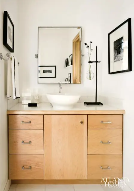 Bathroom vanity with light wood cabinets, white countertop, and a white vessel sink. A silver faucet is mounted on the countertop.