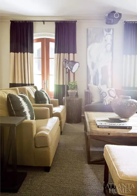 Living room with tan upholstered sofas, black and tan striped curtains, a large painting of a white horse, and a wooden coffee table with a book on it.