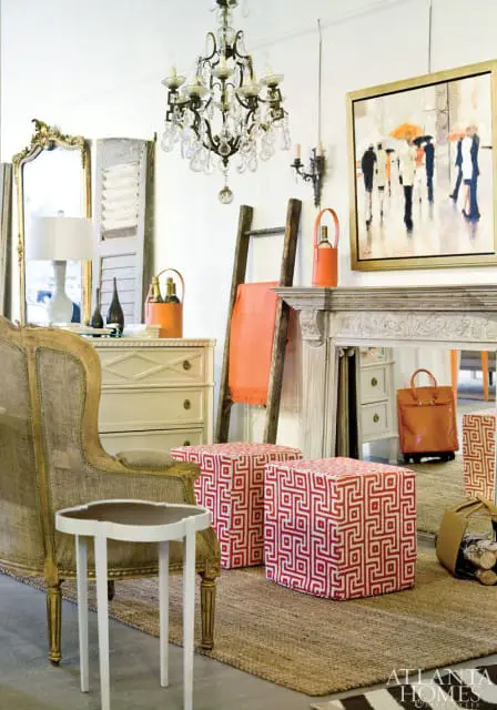 Living room vignette with a vintage armchair, cream dresser, ornate fireplace, and two red and white geometric ottomans.