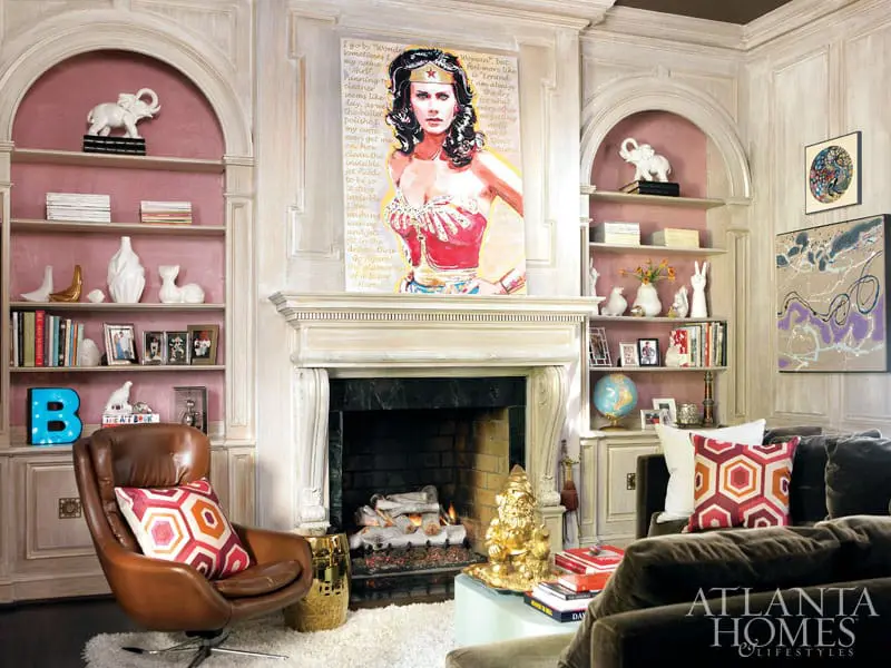 Living room with built-in bookshelves flanking a fireplace, featuring a Wonder Woman painting, leather armchair, and plush sofa.