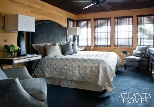 Bedroom with wood-paneled walls and ceiling, king-size bed with a dark upholstered headboard and a white quilted coverlet, blue carpet, and a ceiling fan.